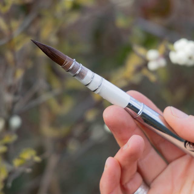 A hand holding a sturdy mop brush with a blurry background of snowberries.